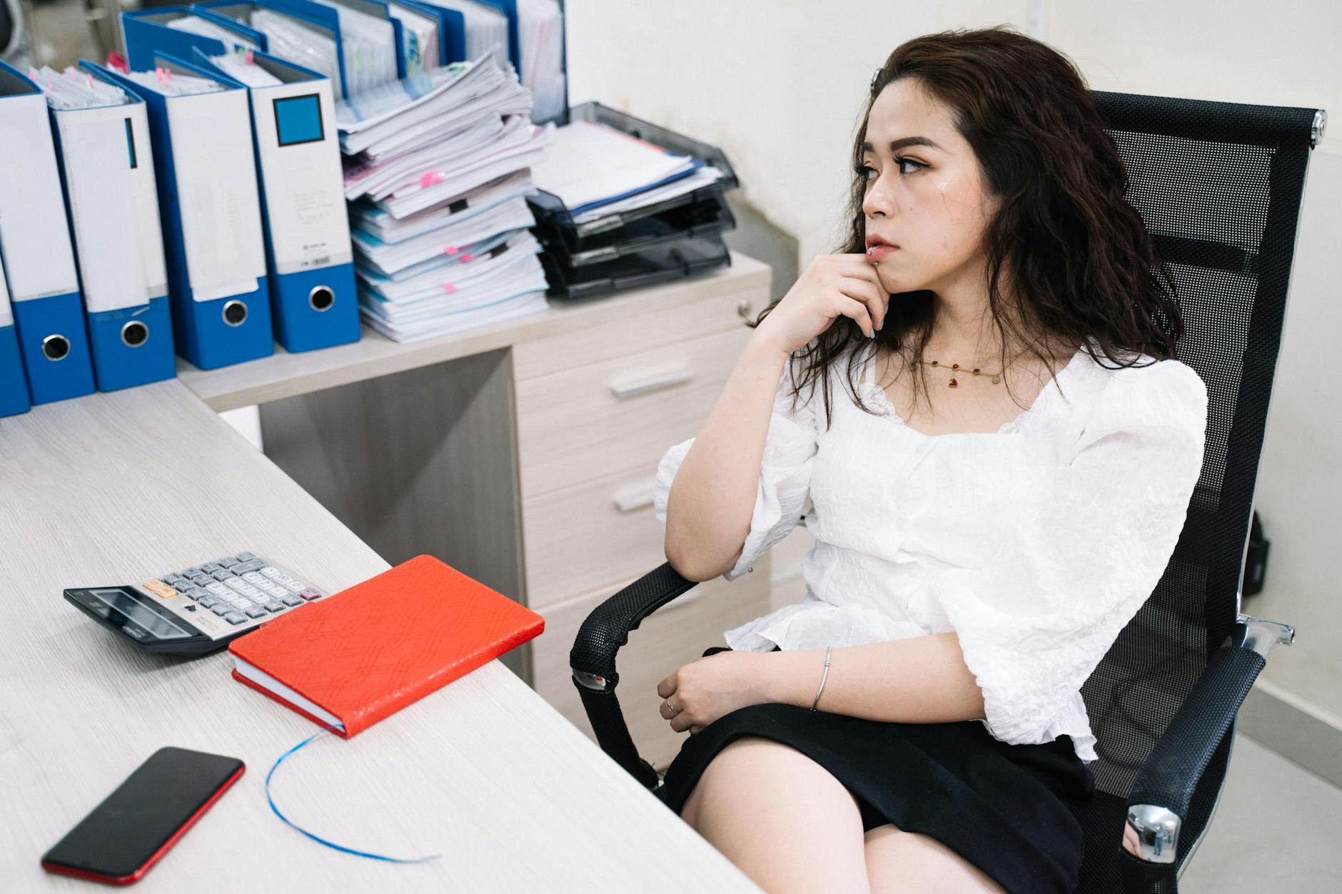 Azjatka przy biurku w pracy, zamyślona nad ekranem laptopa