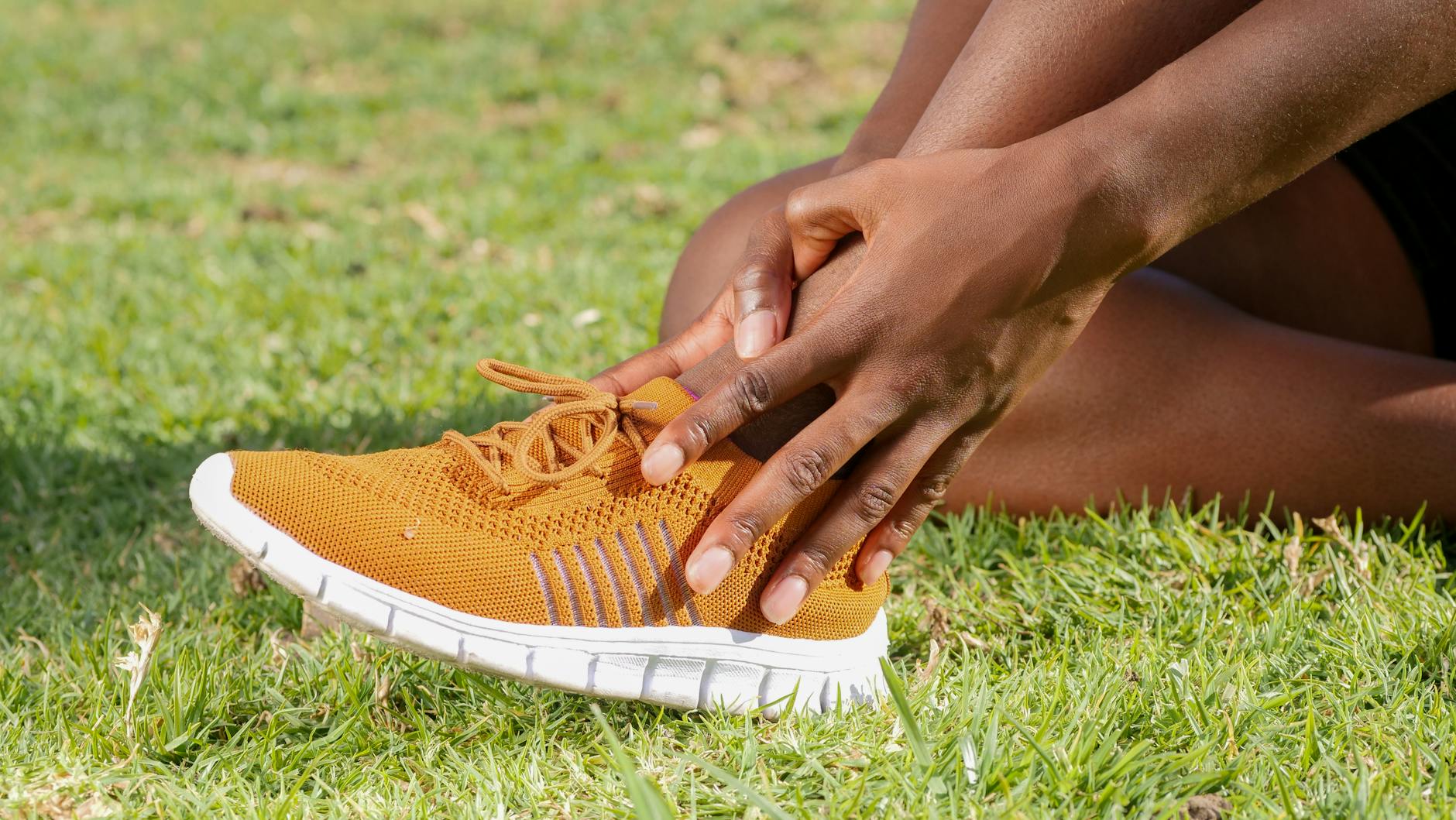 Osoba w pomarańczowym bucie trzyma bolącą skręconą kostkę