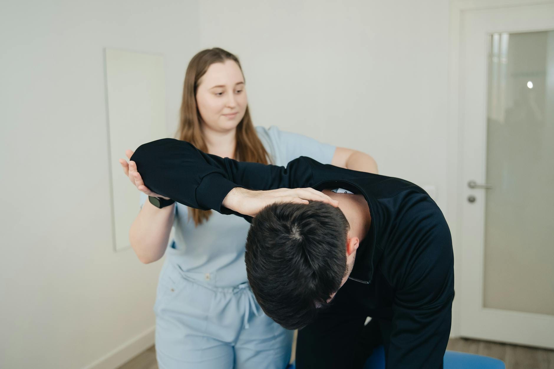 Fizjoterapeuta pomaga pacjentowi w ćwiczeniu rozciągającym szyję