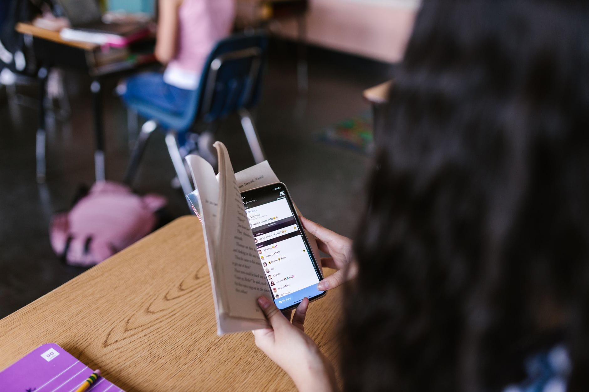 Uczeń w klasie jednocześnie czyta książkę i korzysta ze smartfona